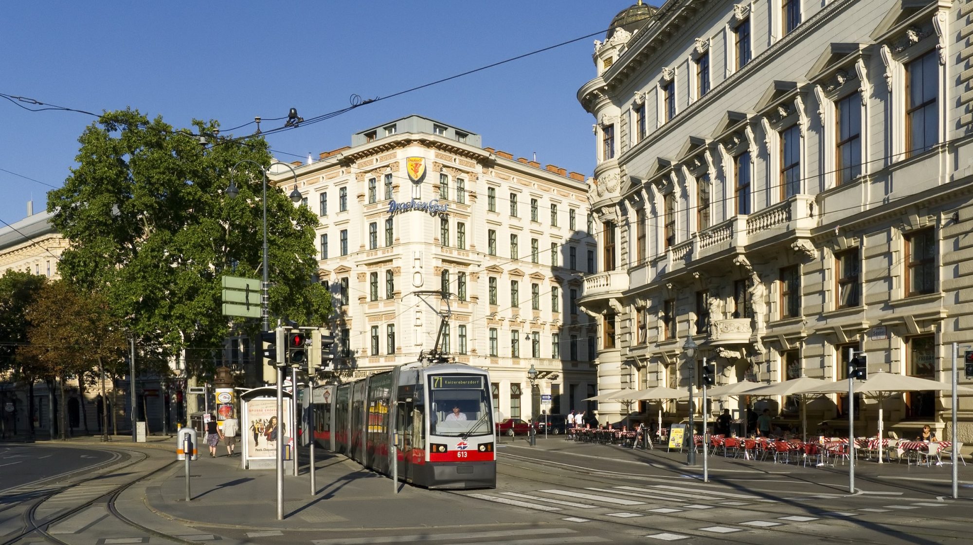 A red Vienna tram on the Ringstrasse, passing the grand facades and pavement cafes of the Schubertring