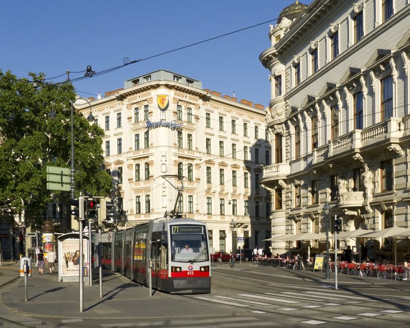 A red Vienna tram on the Ringstrasse, passing the grand facades and pavement cafes of the Schubertring