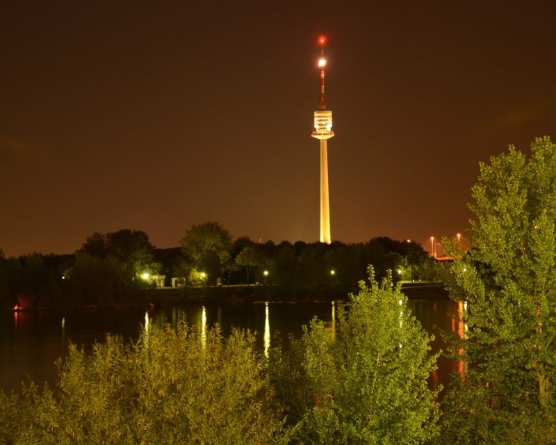 The Danube Tower lit up at night, reflected in the water below