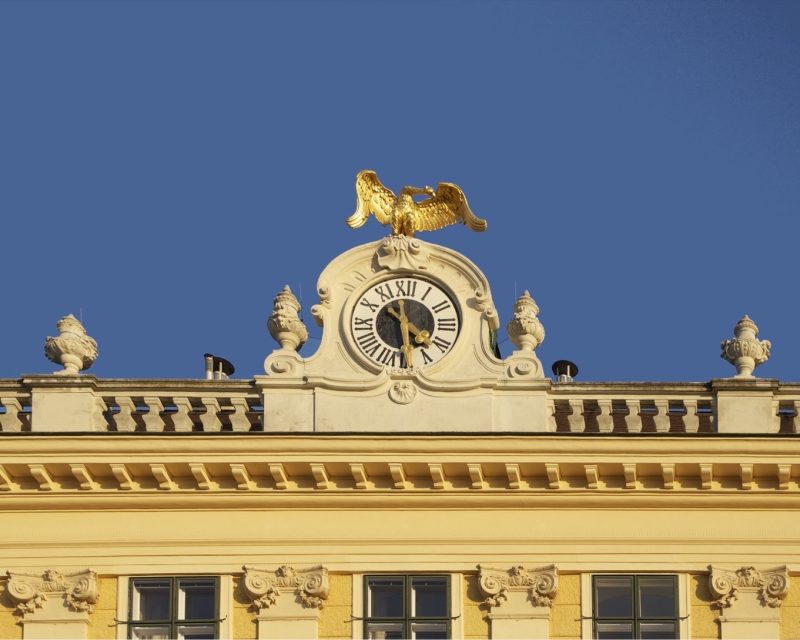 The gilded clock and imperial eagle on Schönbrunn's west roofline against a blue sky