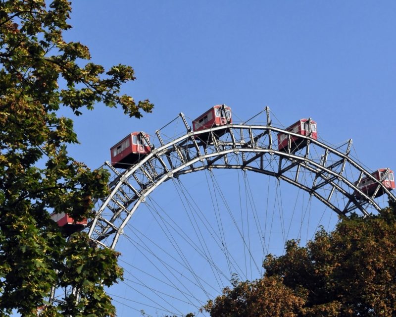 The Riesenrad's red gondolas and steel spokes framed by summer trees