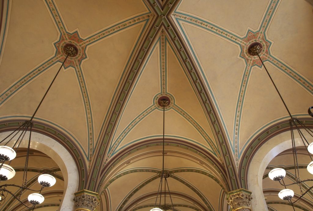 The vaulted ceiling of a Viennese coffee house, its arches lit by hanging lamps