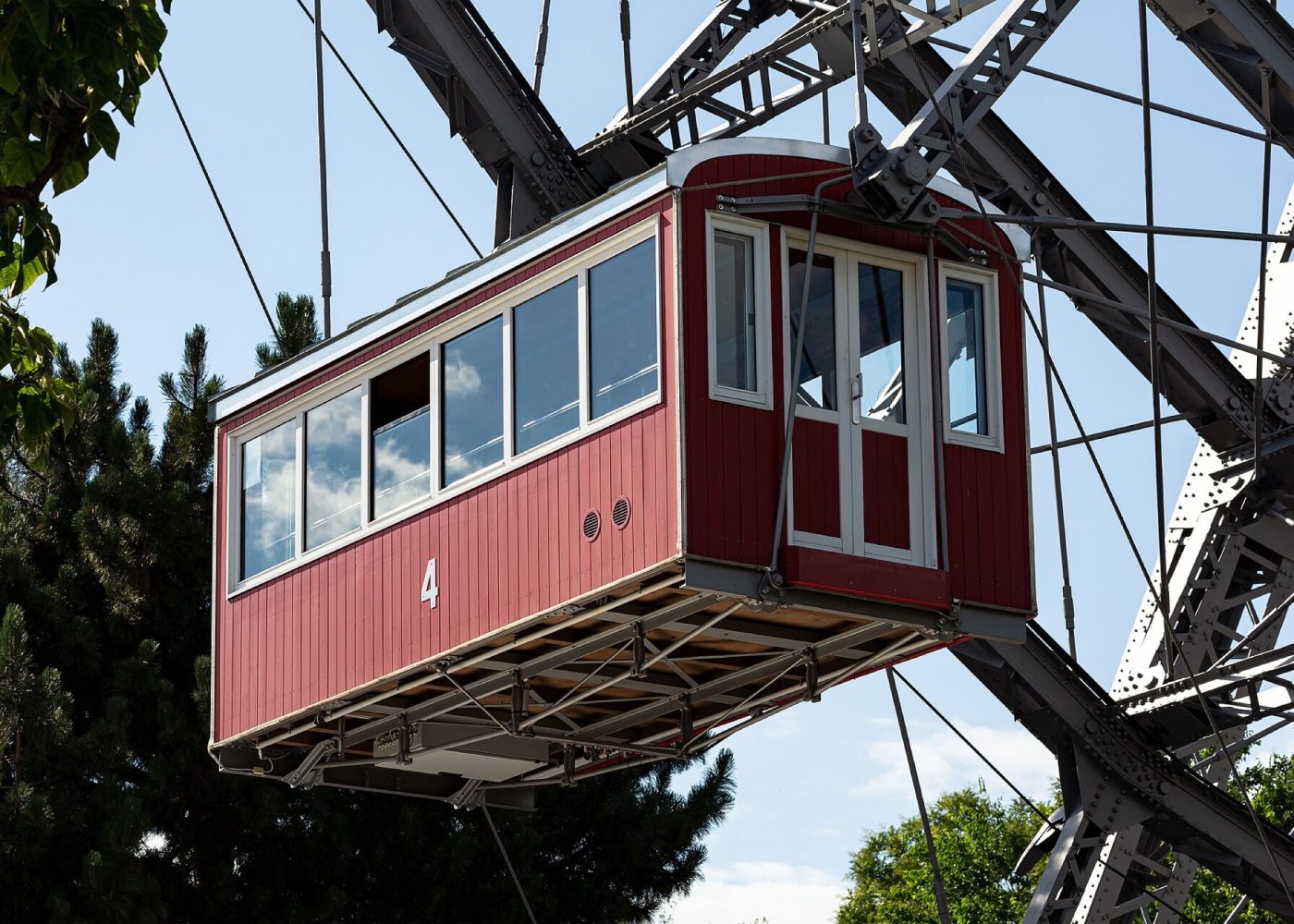 A red wooden gondola of the Wiener Riesenrad against a blue sky, with the wheel's steel structure behind it